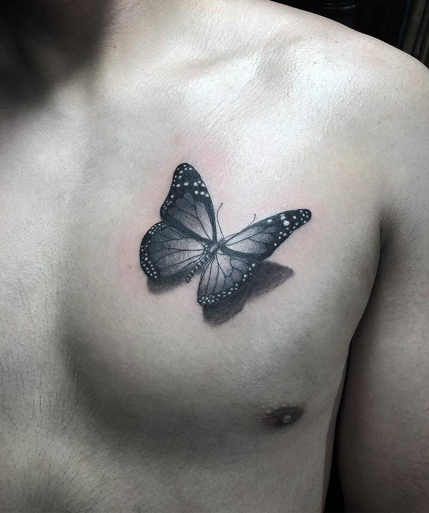 A black and white butterfly tattoo, reminiscent of a monarch, graces a person's chest with its detailed wing patterns and intricate shading