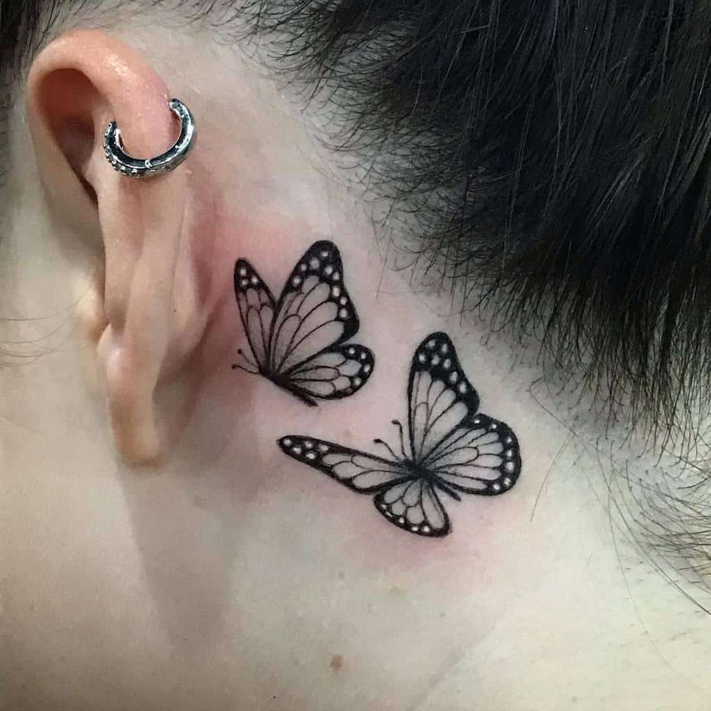 Two black butterfly tattoos resembling monarchs behind the ear