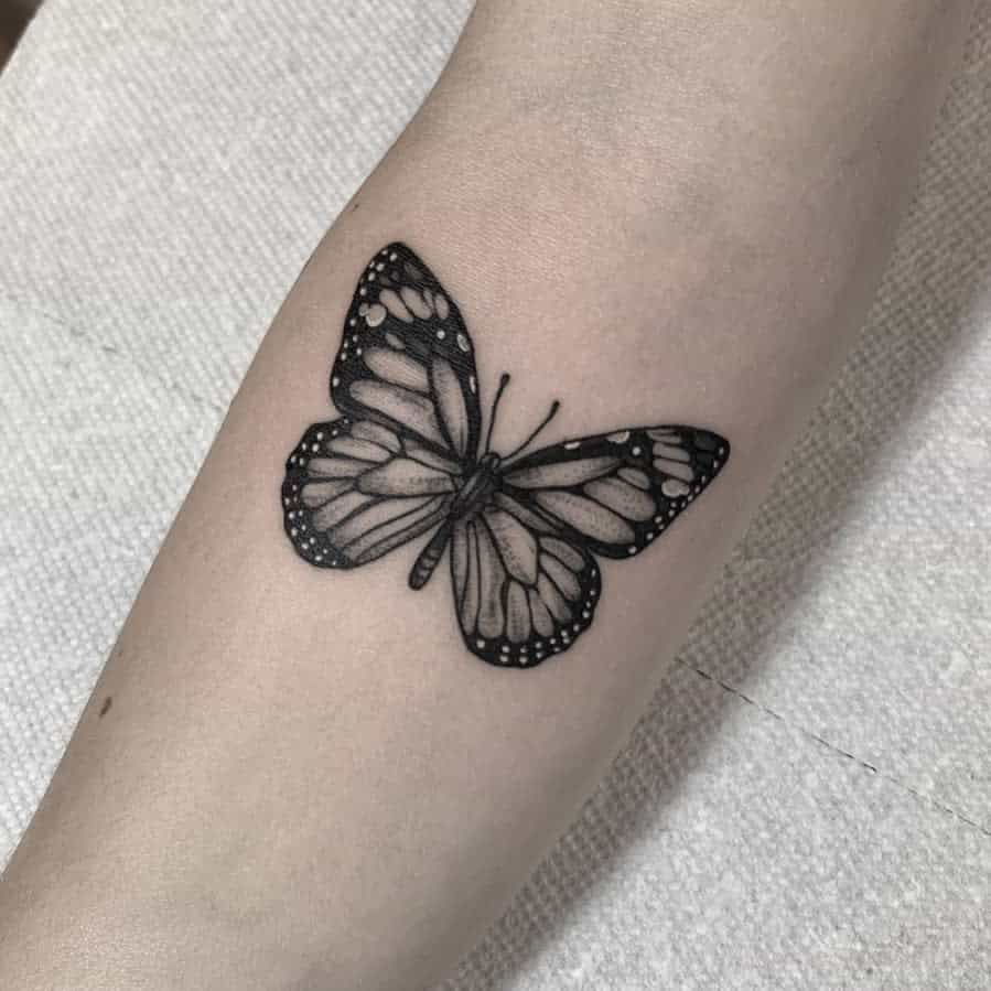 A black and white monarch butterfly tattoo on a orearm, its wings intricately detailed with exquisite shading
