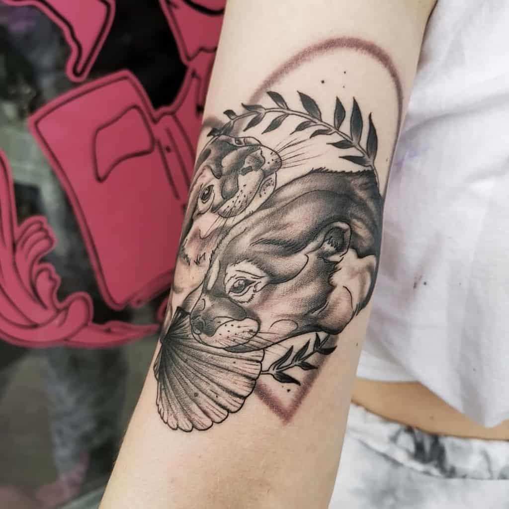 Detailed black and grey tattoo of otters with leaves and a seashell, featuring fine shading and a soft geometric frame