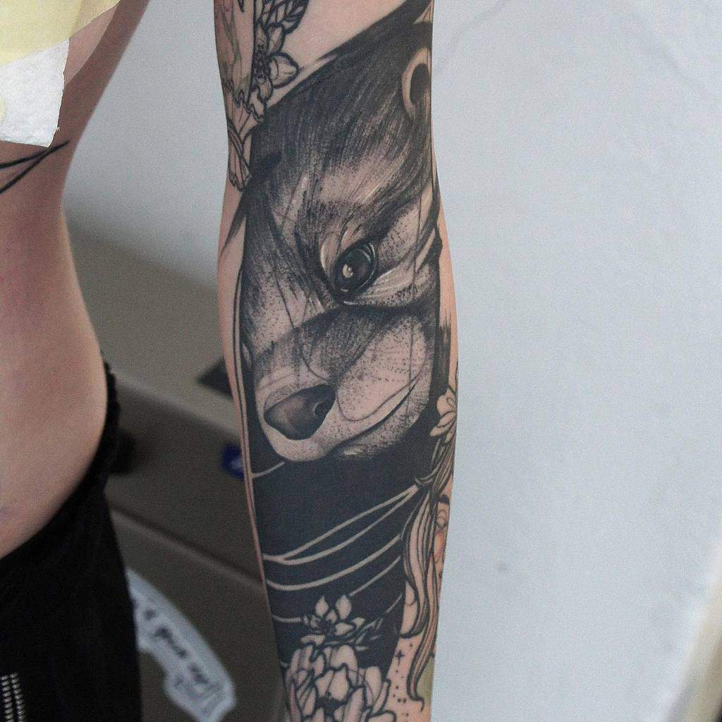 Forearm tattoo featuring a detailed bear and otter face with floral designs surrounding them