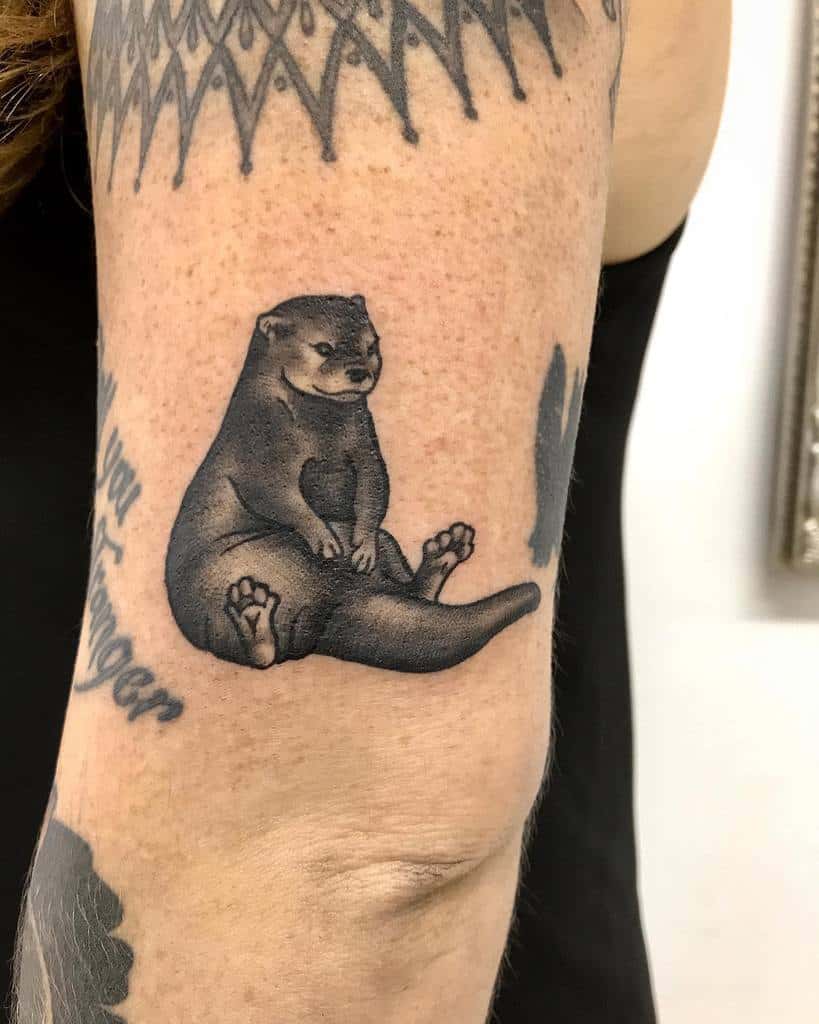 A detailed tattoo of a sitting otter adorns an arm, seamlessly blending with surrounding ink
