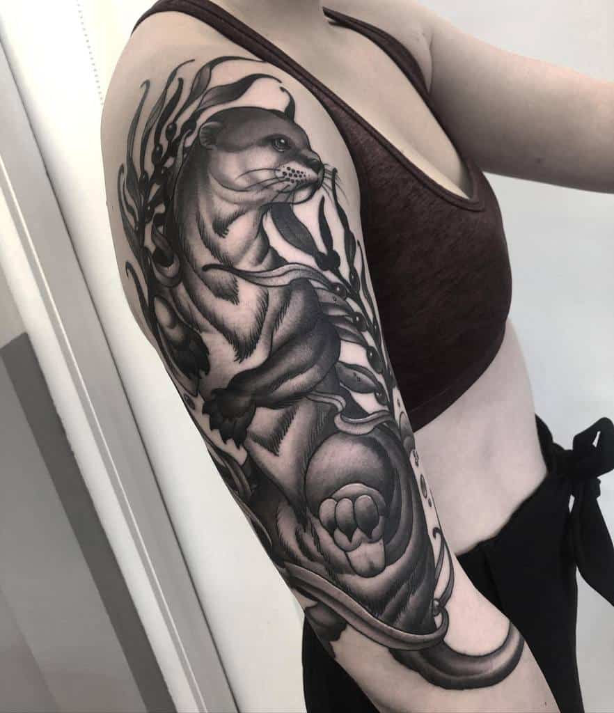 Black and white otter tattoo with flowing lines and intricate details adorns a person's upper arm