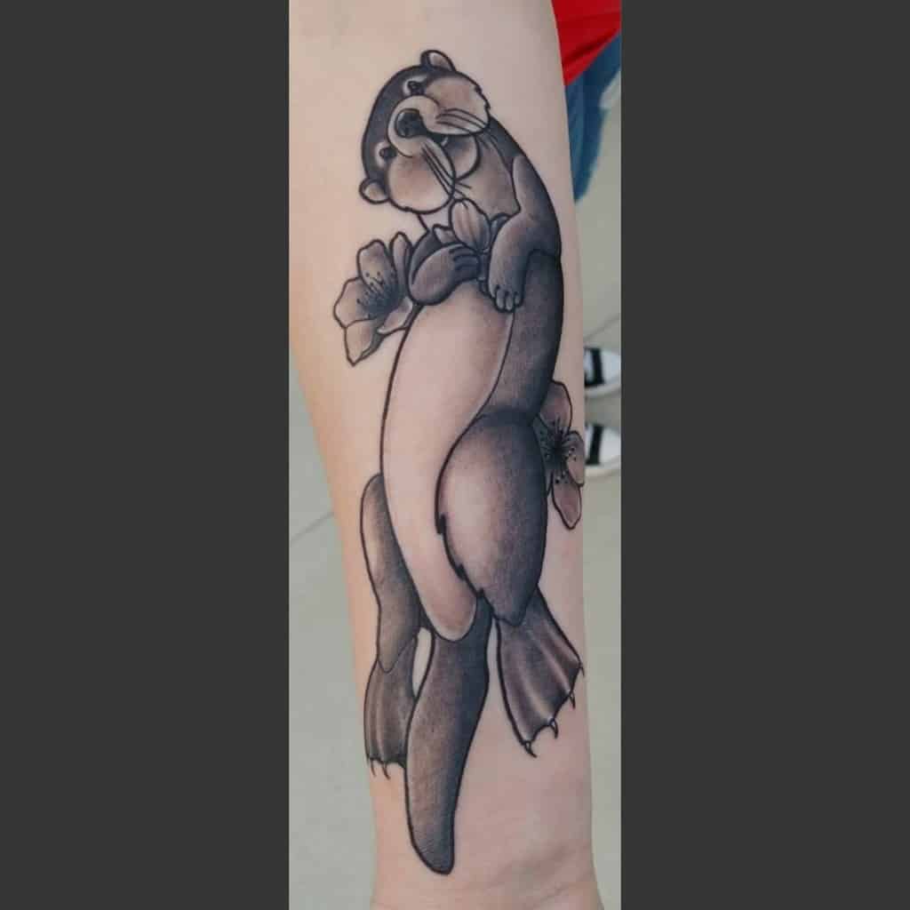 Tattoo of a playful otter gently cradling vibrant flowers on a person's arm