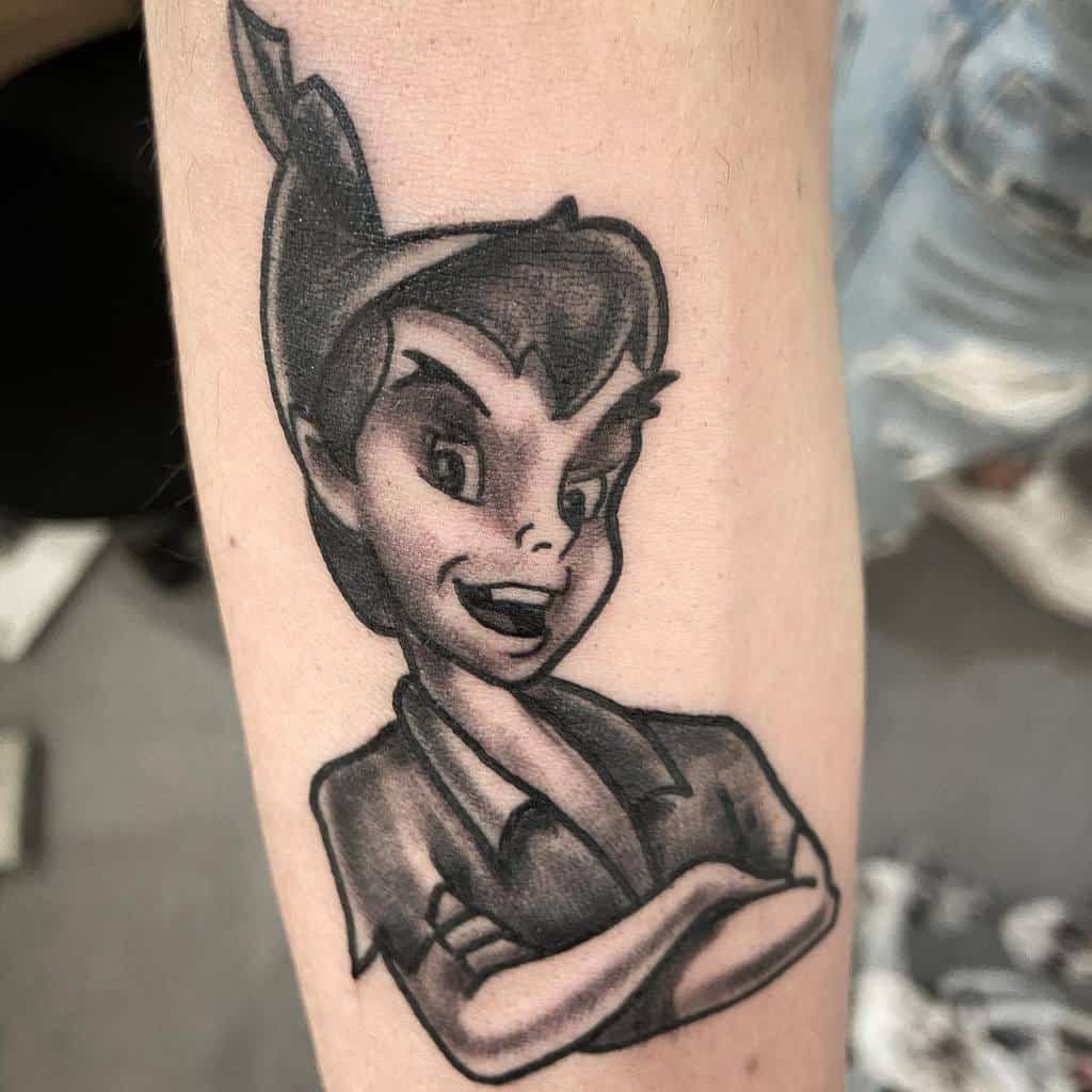 Black and gray tattoo of Peter Pan with a confident expression, arms crossed, showcasing bold shading and classic design