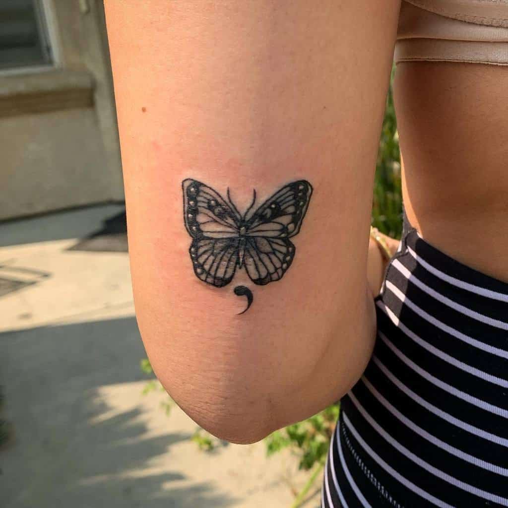 A delicate black semicolon butterfly tattoo on the back of the arm, symbolizing perseverance, mental health awareness, and the journey of overcoming challenges