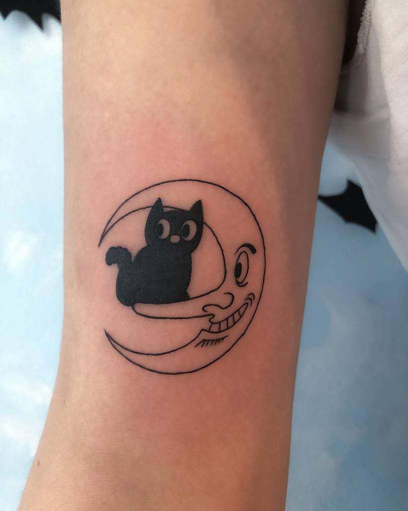 Tattoo of a black cat sitting on a crescent moon with a face