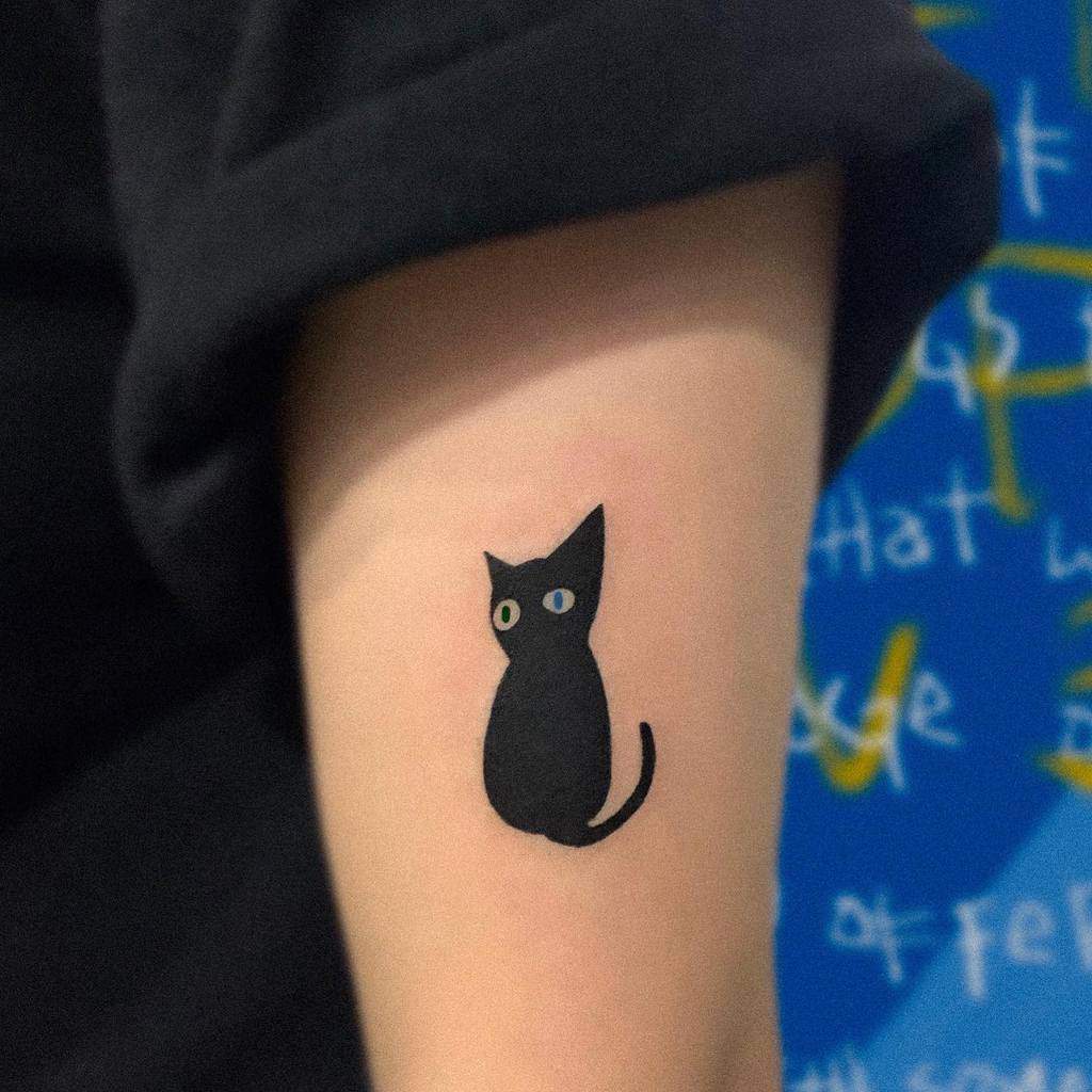 Tattoo of a black cat silhouette with yellow eyes on a person's arm