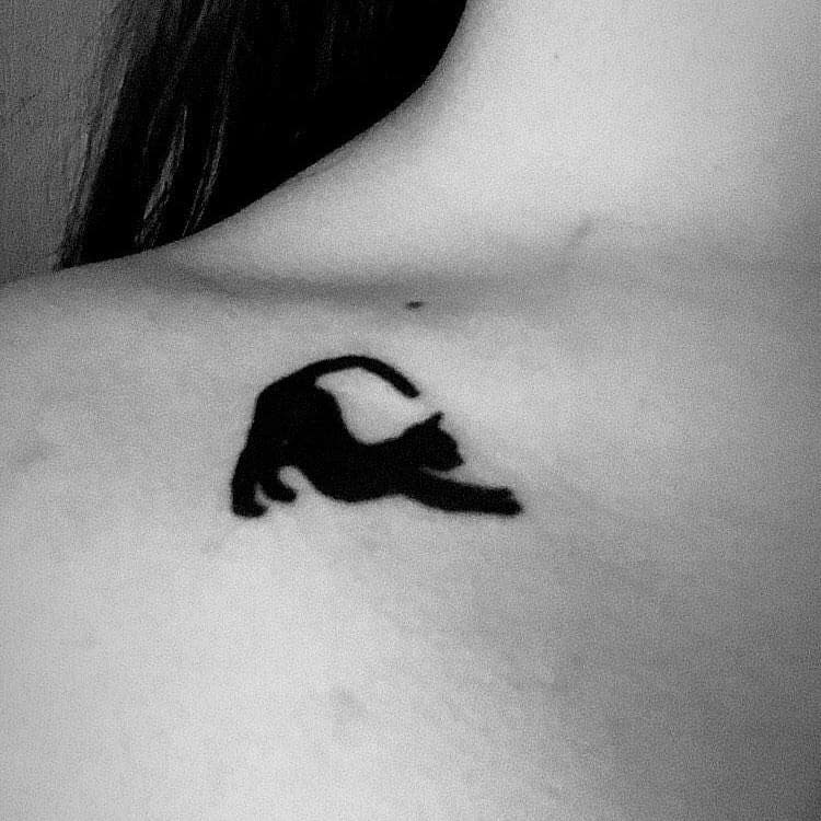 Silhouette tattoo of a stretching cat on a shoulder