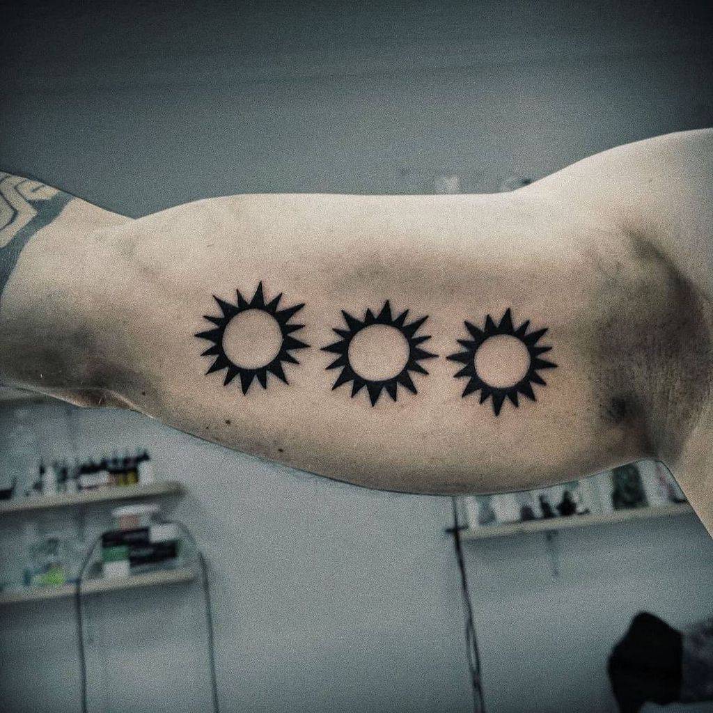 Three black sun tattoos on a person's bicep