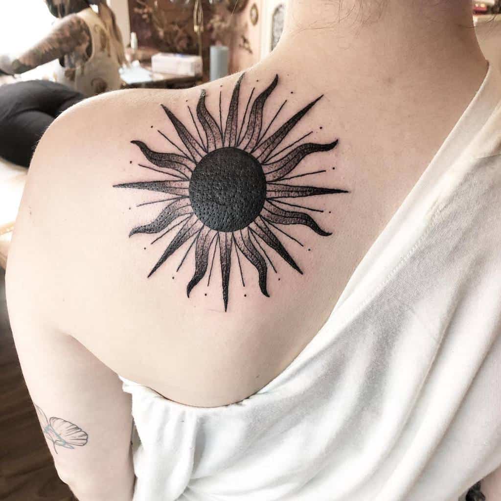 Tattoo of a sun with wavy rays on a person's upper back
