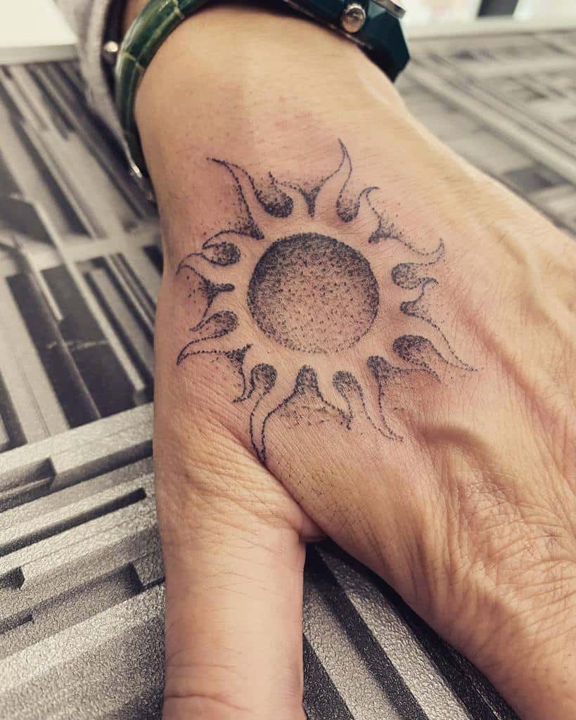 Intricate sun tattoo on the wrist, featuring a detailed core with dynamic, flame-like rays extending outward