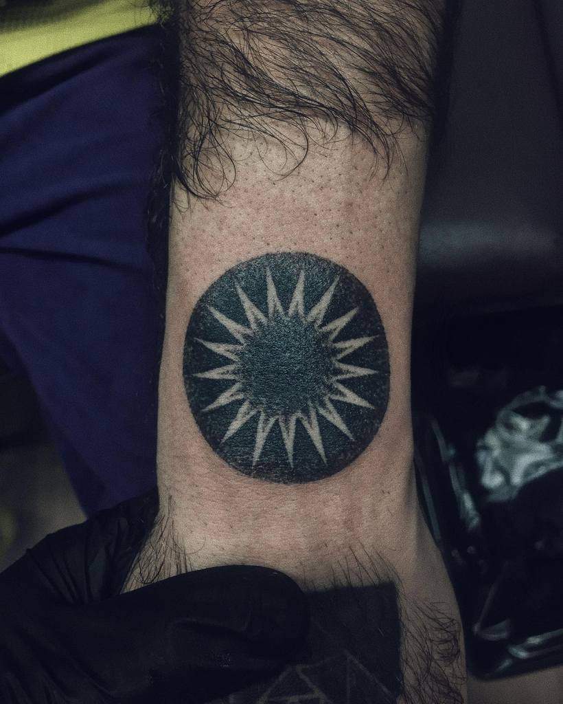 Sun tattoo with white starburst design on forearm
