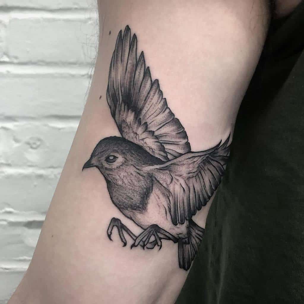 Black ink tattoo of a bird in flight on a forearm