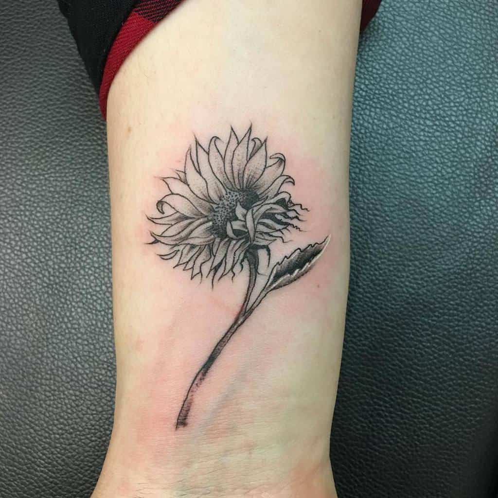 Black and gray sunflower tattoo on a wrist, with detailed petals and stem