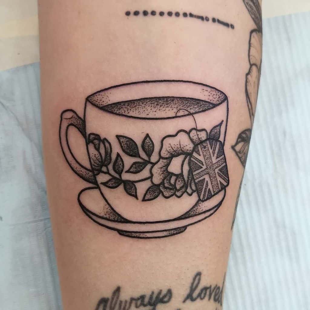 Tattoo of a teacup with flowers and a Union Jack teabag tag, resting on a saucer, symbolizing British tea culture
