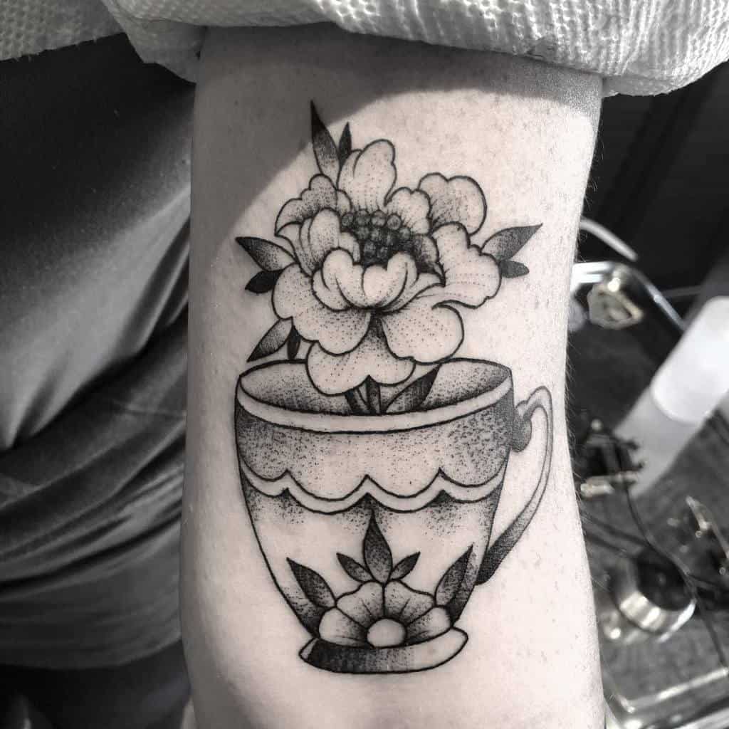 Black tattoo of a flower in a teacup on a person's arm