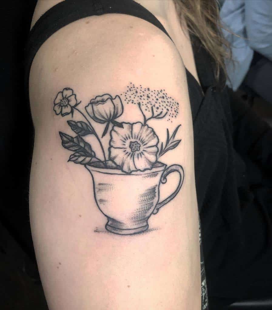 Tattoo of flowers in a teacup, featuring various blooms and leaves in black and gray ink