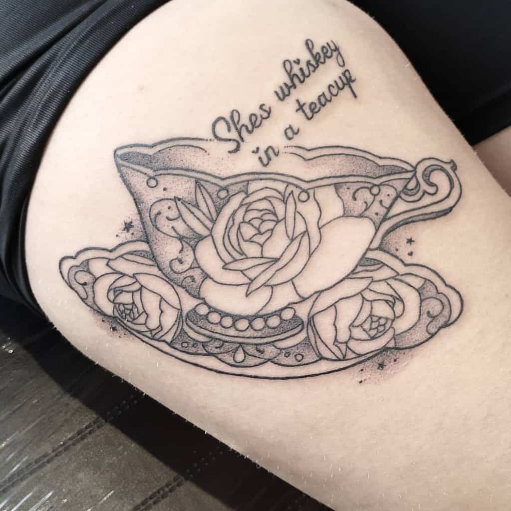 Black tattoo of a teacup with roses and the phrase "She's whiskey in a teacup"