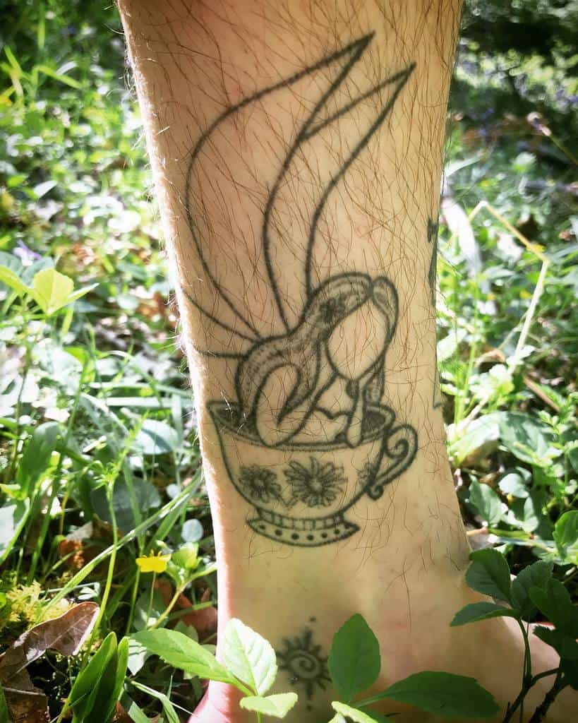 Black and white tattoo of a fairy with large wings sitting inside a decorated teacup, creating a whimsical and fantasy-inspired design