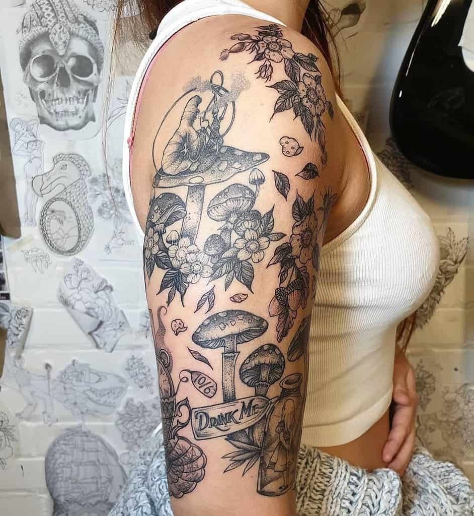 Black and white tattoo featuring Caterpillar from Alice in Wonderland, sitting on a mushroom and surrounded by mushrooms, flowers, nuts and a 'Drink Me' bottle with Alice inside