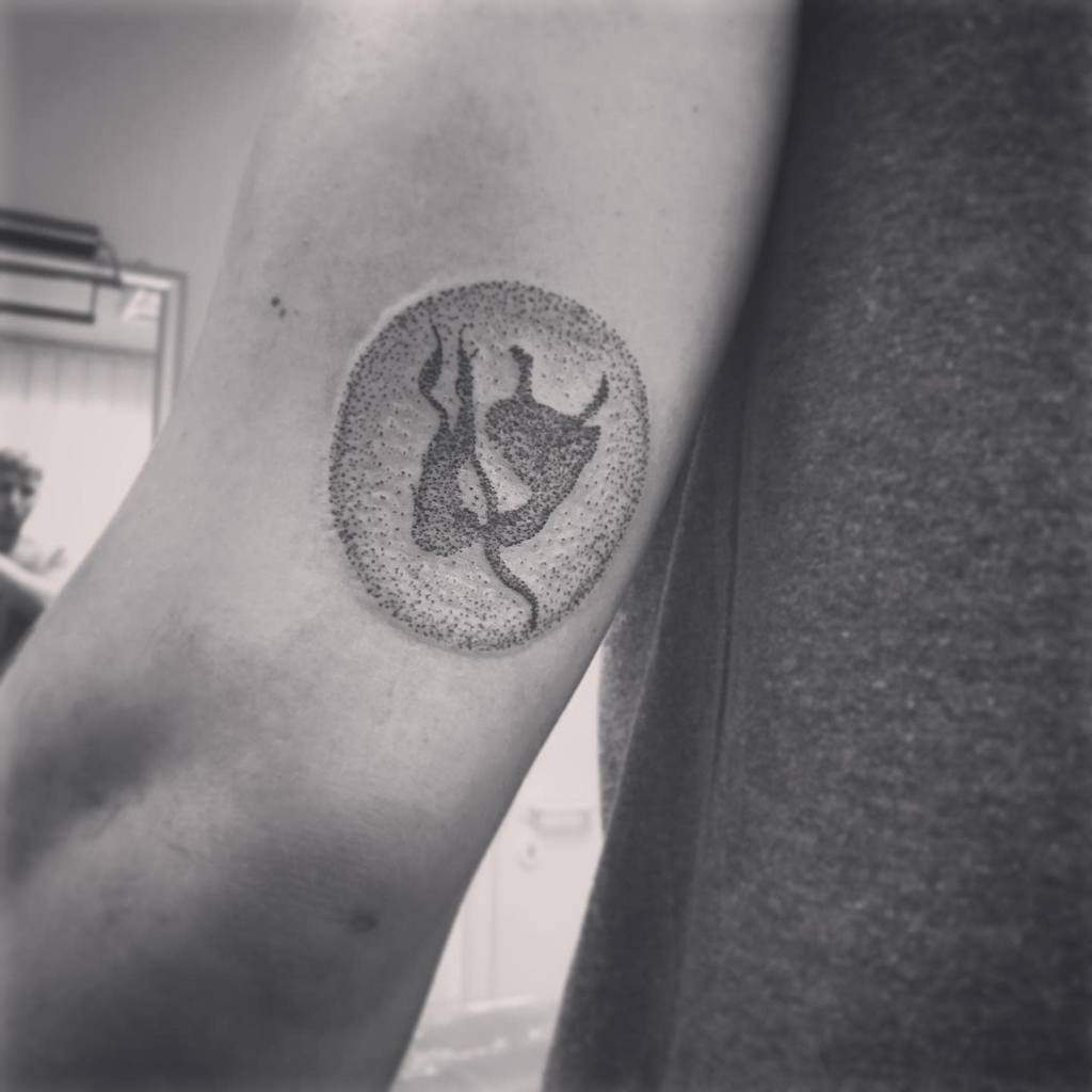 Black and white tattoo of Alice from Alice in Wonderland, surrounded by a dotted circle, with her silhouette depicted as she falls down the rabbit hole