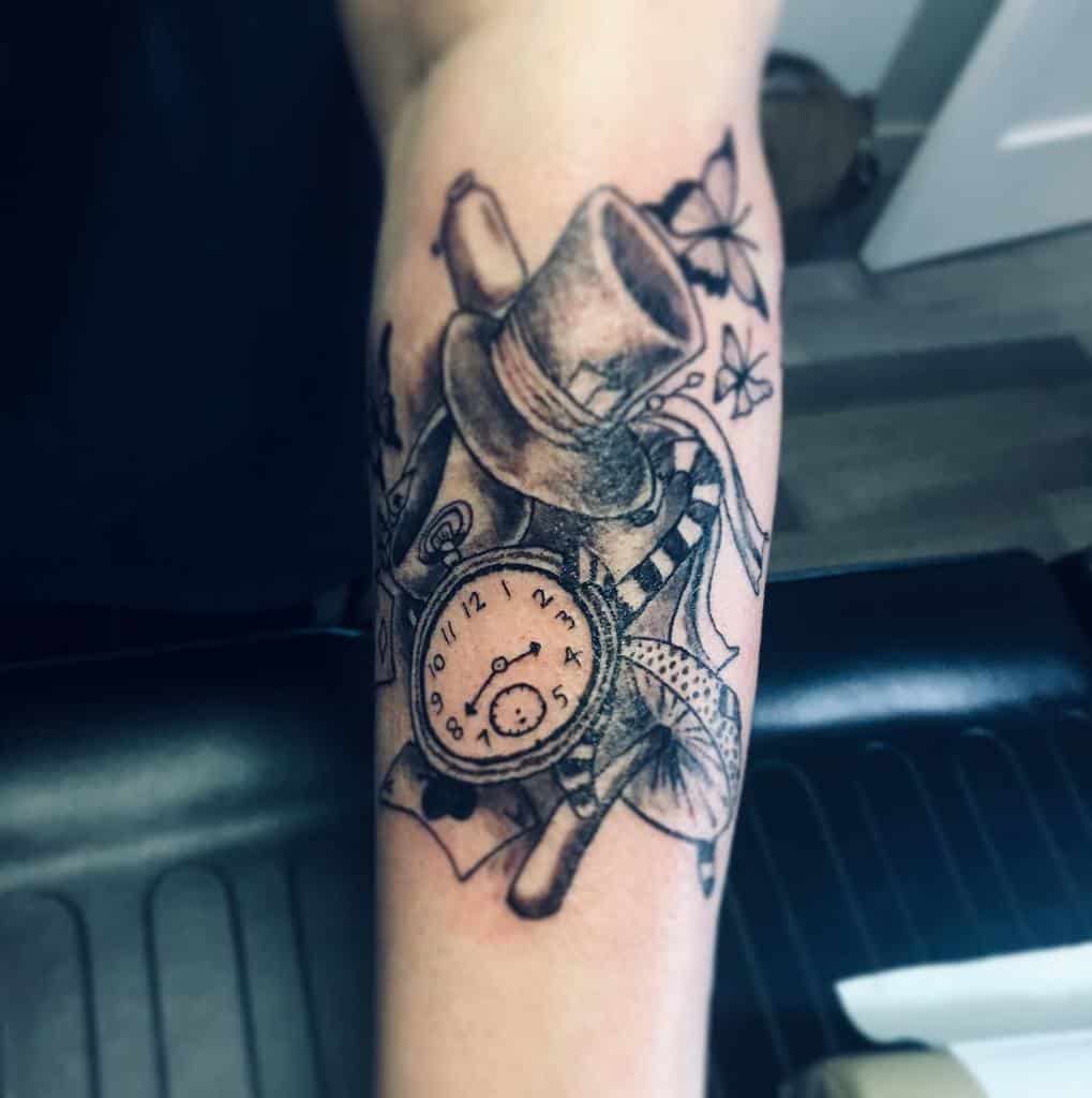 Black and white tattoo of the Mad Hatter’s top hat, a pocket watch, playing cards, candy cane and a butterflies from Alice in Wonderland