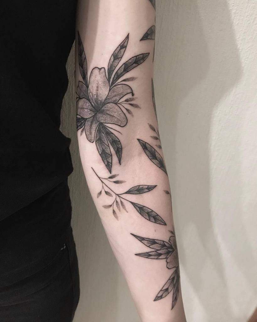 Black and grey tattoo of lilies and leaves with fine shading and geometric details, creating a bold yet elegant botanical design