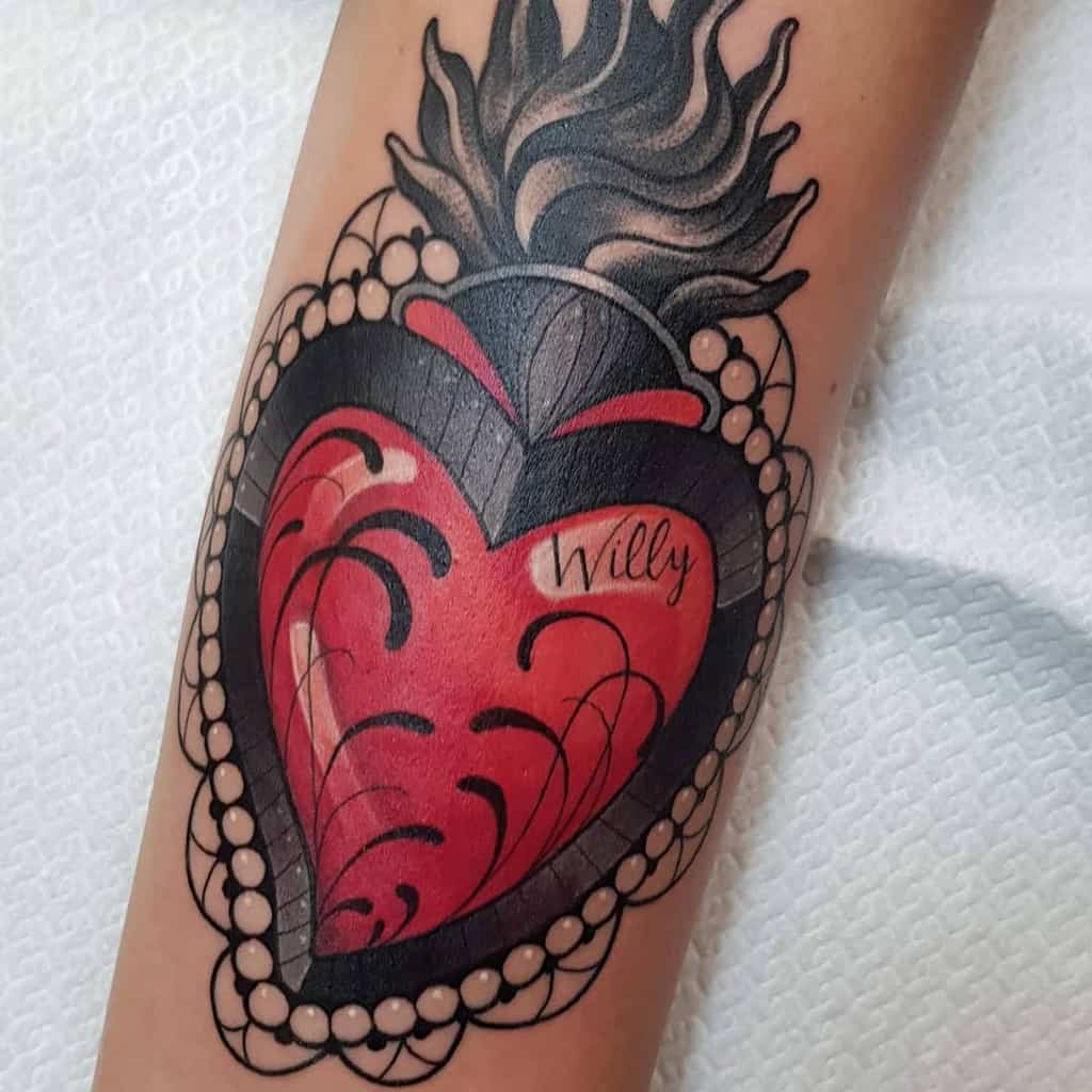 Ornate Sacred Heart tattoo with black flames, decorative pearl border, and a red heart inscribed with 'Willy' in elegant script