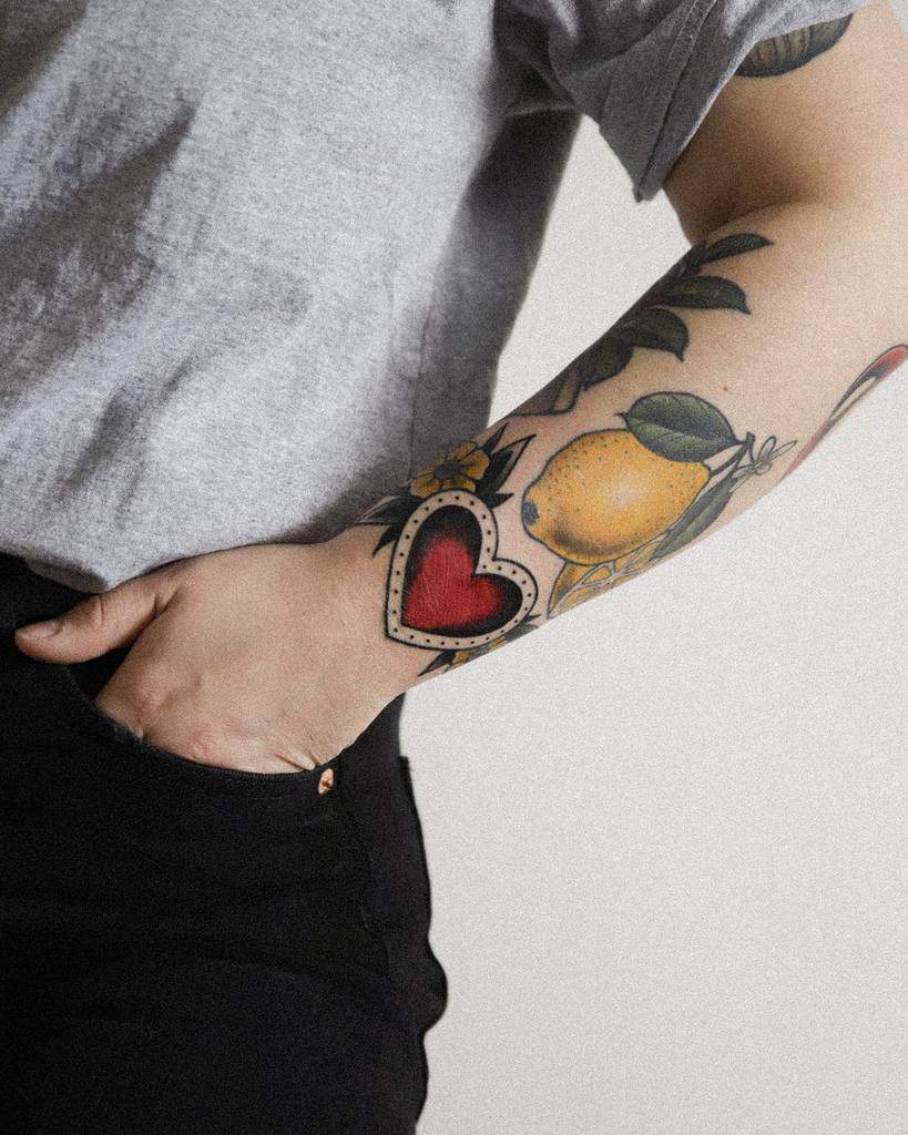 Colorful tattoos of a red heart and a lemon with leaves