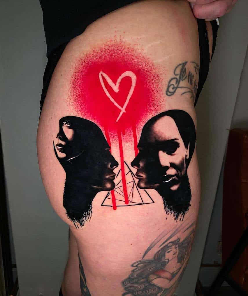 Bold black and red tattoo featuring two abstract faces, a geometric pyramid, and a dripping graffiti-style heart on a red spray-painted background