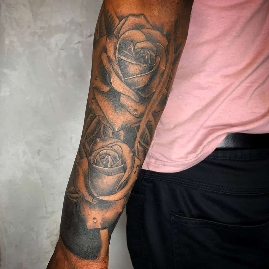 Black and gray sleeve tattoo featuring two detailed roses with layered petals and leaves, creating a bold yet elegant design