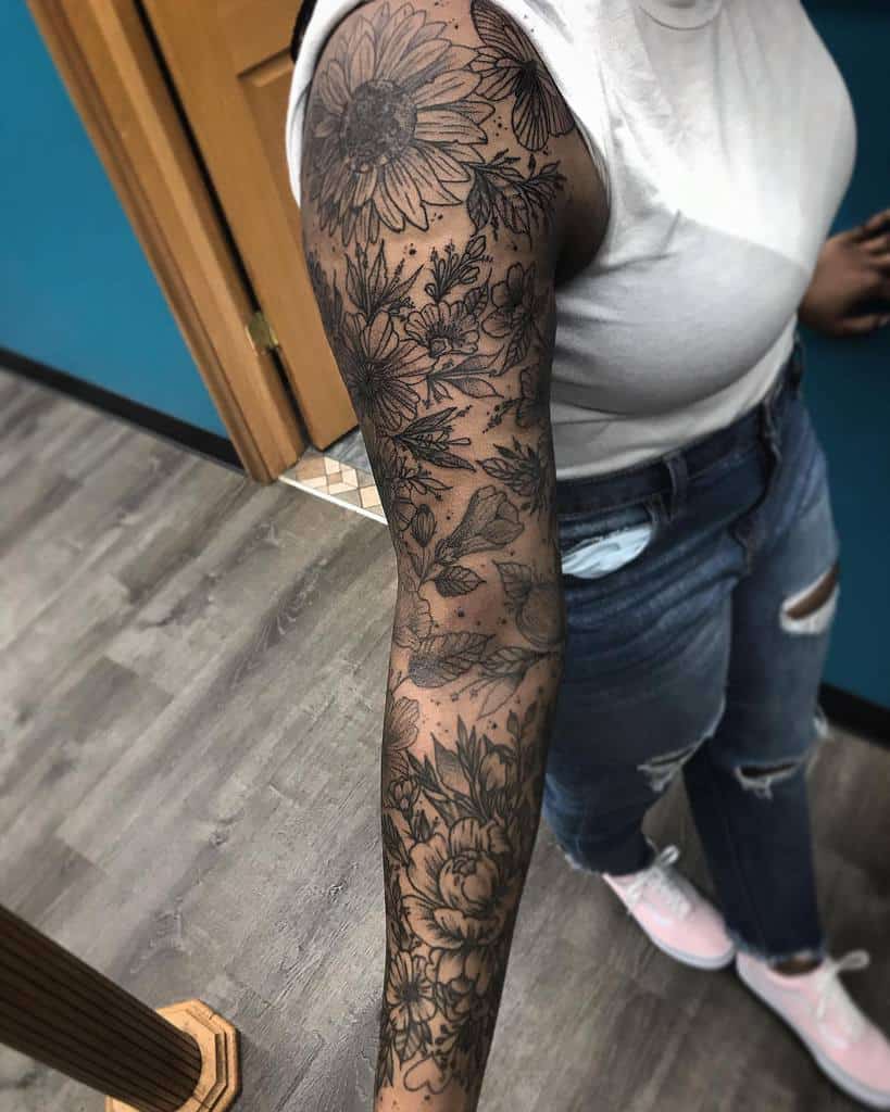 Intricate black and white floral tattoo sleeve featuring sunflowers, roses, and delicate leaves, accented with butterflies