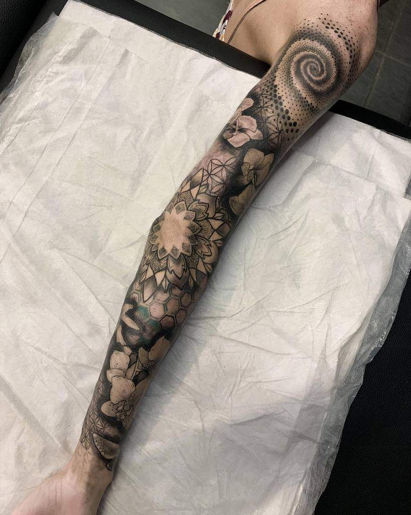 Intricate black and white full sleeve tattoo combining geometric patterns, floral designs, and a striking spiral motif near the shoulder for a modern and artistic look