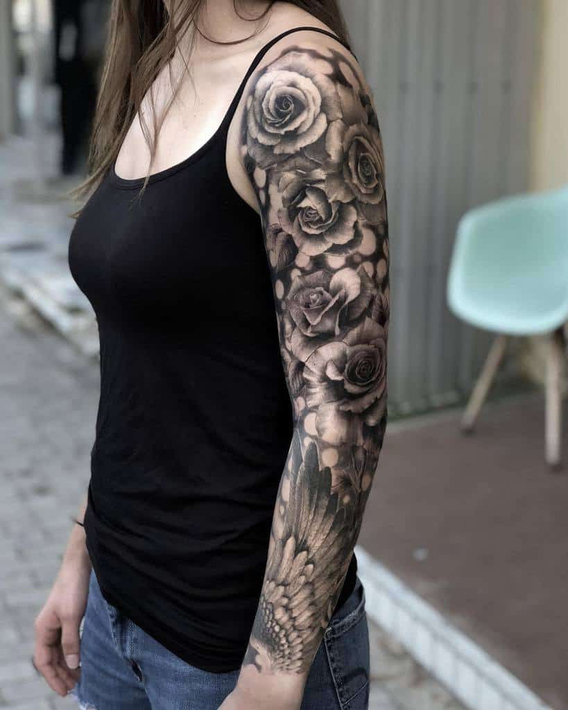 Woman with a sleeve tattoo of roses and feathers on her arm