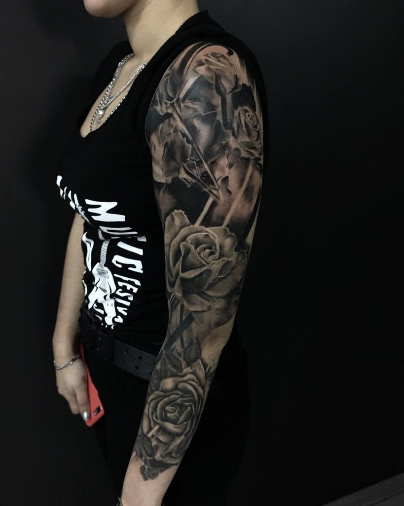 A woman with a detailed black rose sleeve tattoo on her arm