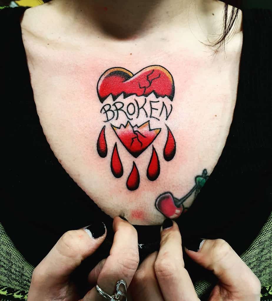 Tattoo of a bleeding heart with dripping blood and the word "BROKEN" on a person's chest