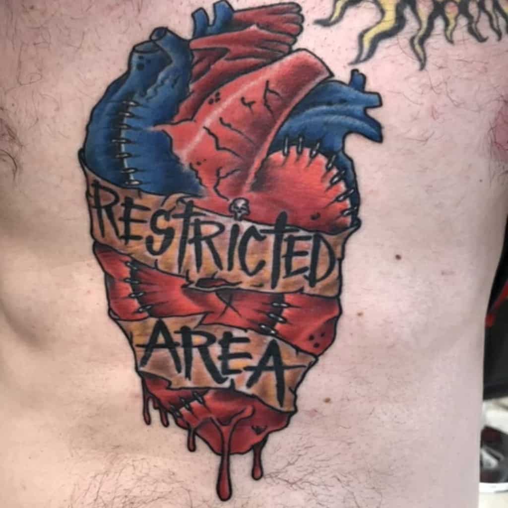A colorful anatomical heart tattoo on a chest, with the words "Restricted Area" written on it, features intricate details that appear almost bleeding into the surrounding skin