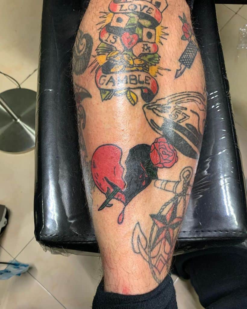 Leg tattoo featuring a bleeding broken heart, roses, dice, and other various designs on a person's calf