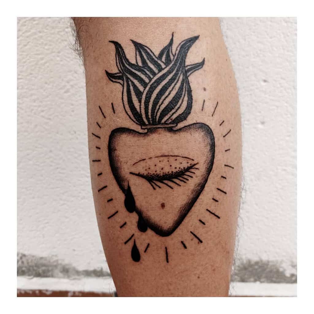 Tattoo of a bleeding heart with an eye, flames, and teardrops on an individual's leg