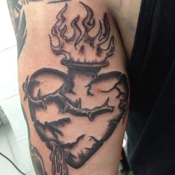 Tattoo of a heart with flames, barbed wire, and subtle bleeding on an upper arm