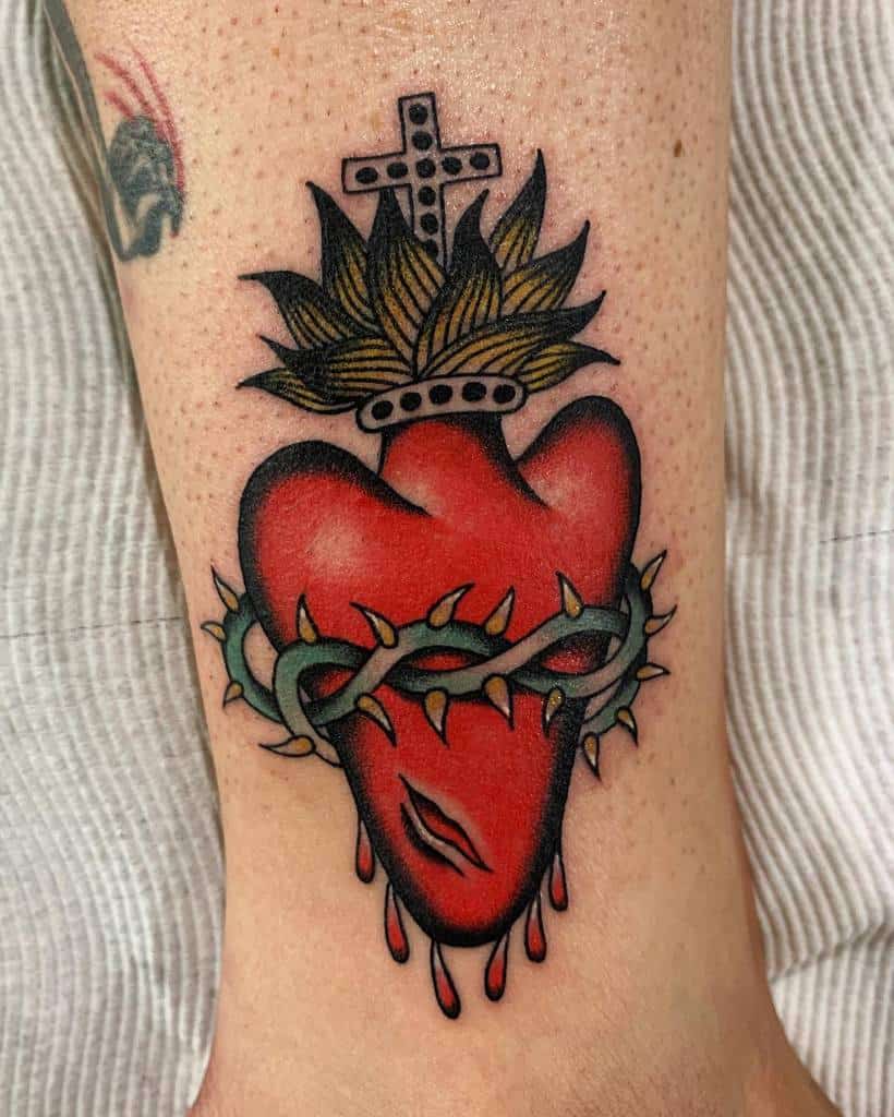 Tattoo of a bleeding Sacred Heart with thorns, flames, and a cross on a person's leg