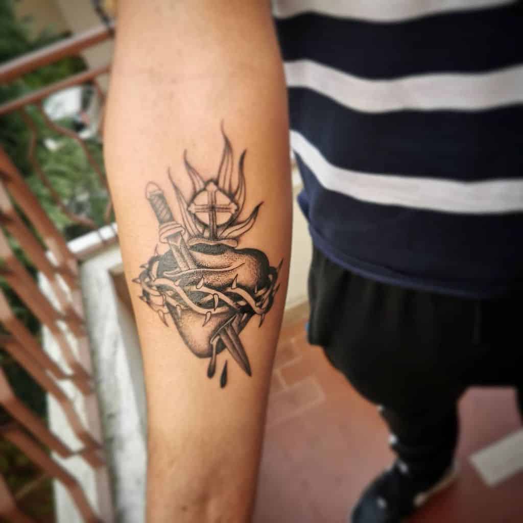 Tattoo of a flaming heart pierced by a sword and thorns, bleeding on a person's forearm