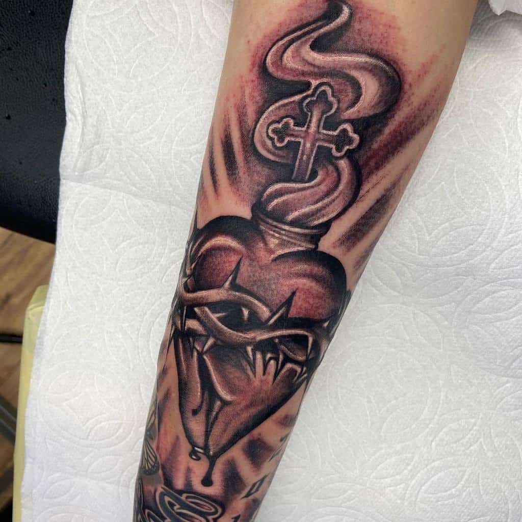 Tattoo of a bleeding heart with thorns, a flaming cross, and swirling smoke on a person's arm