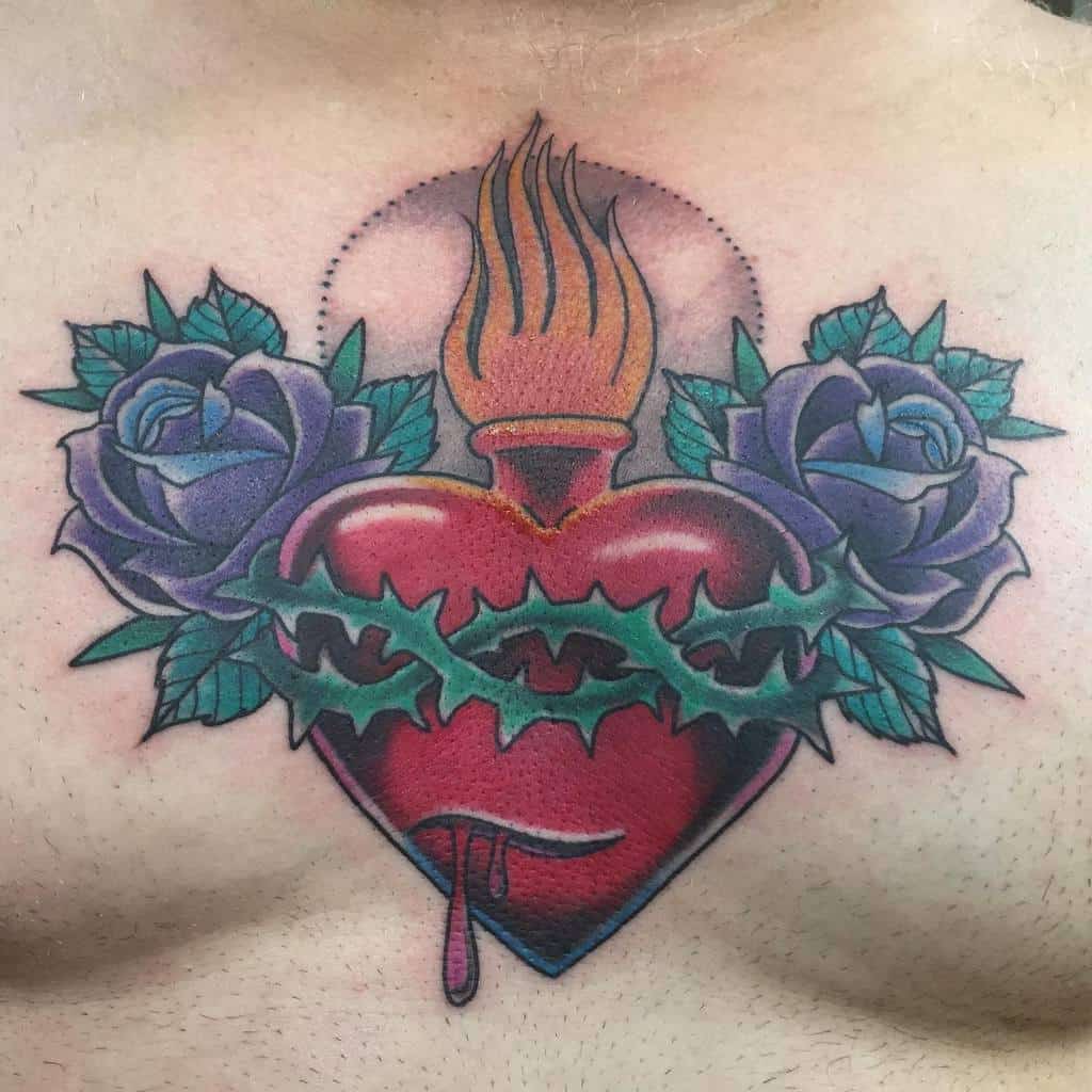 Tattoo of a flaming, bleeding heart wrapped in thorns and flanked by two blue roses on a chest