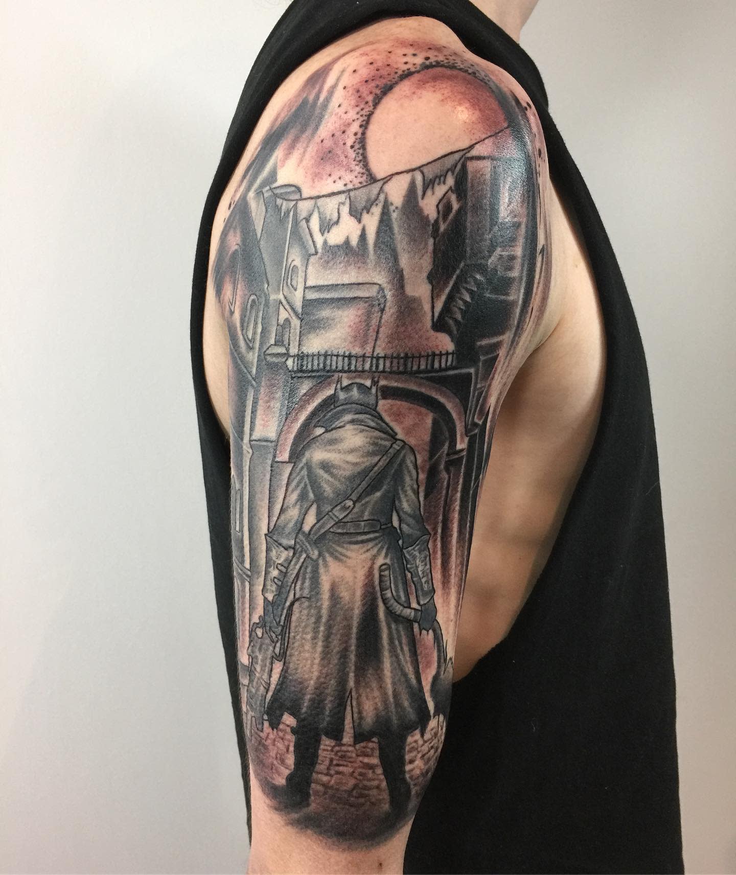 Upper arm tattoo of a Bloodborne hunter standing under a gothic archway with a blood-red moon