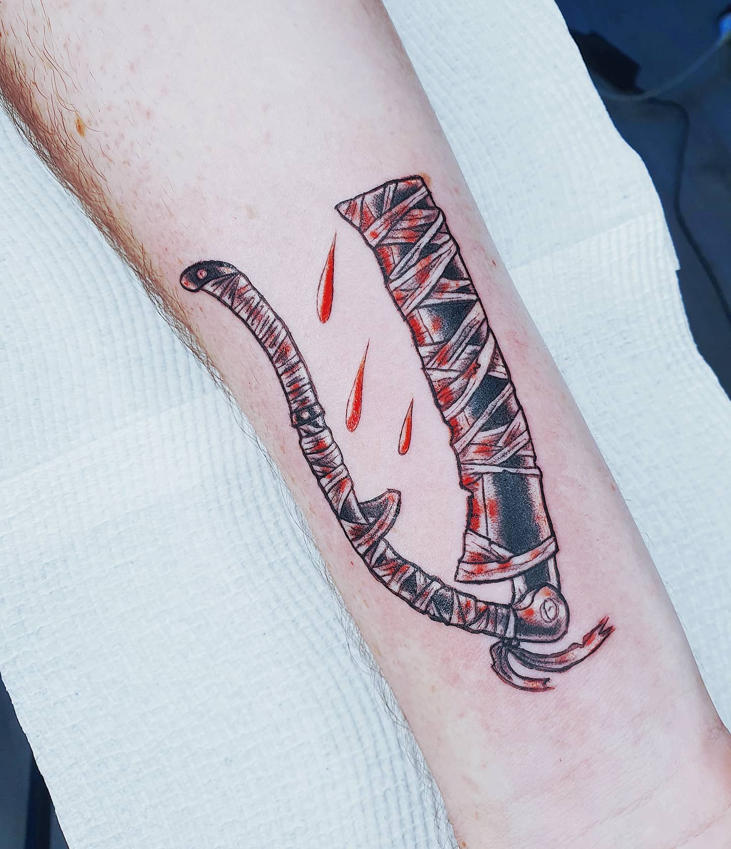 Tattoo featuring the iconic Bloodborne saw cleaver with blood splatters, wrapped in bandages