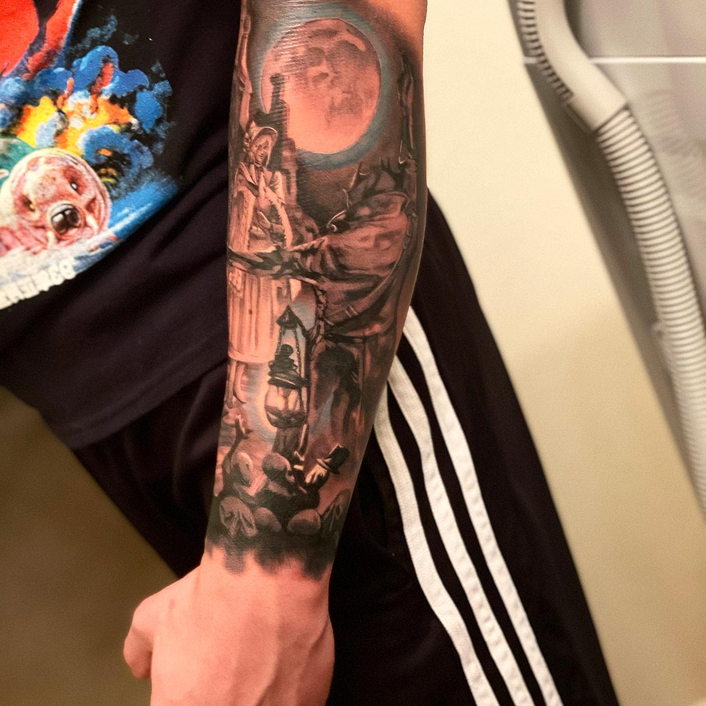 Forearm tattoo of a Bloodborne hunter under a blood-red moon with gothic architecture and skulls