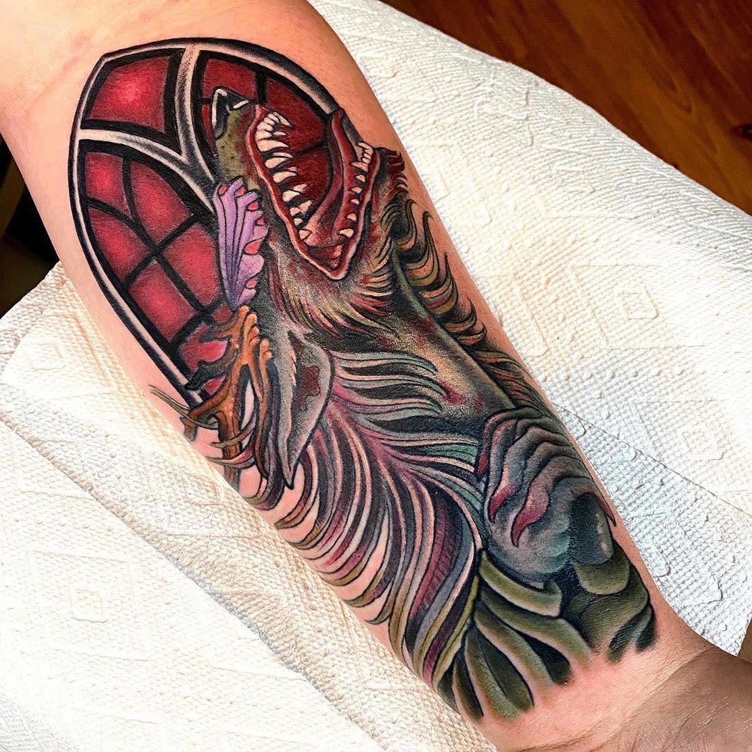 Forearm tattoo featuring a colorful, fierce Bloodborne creature with a red-stained glass background