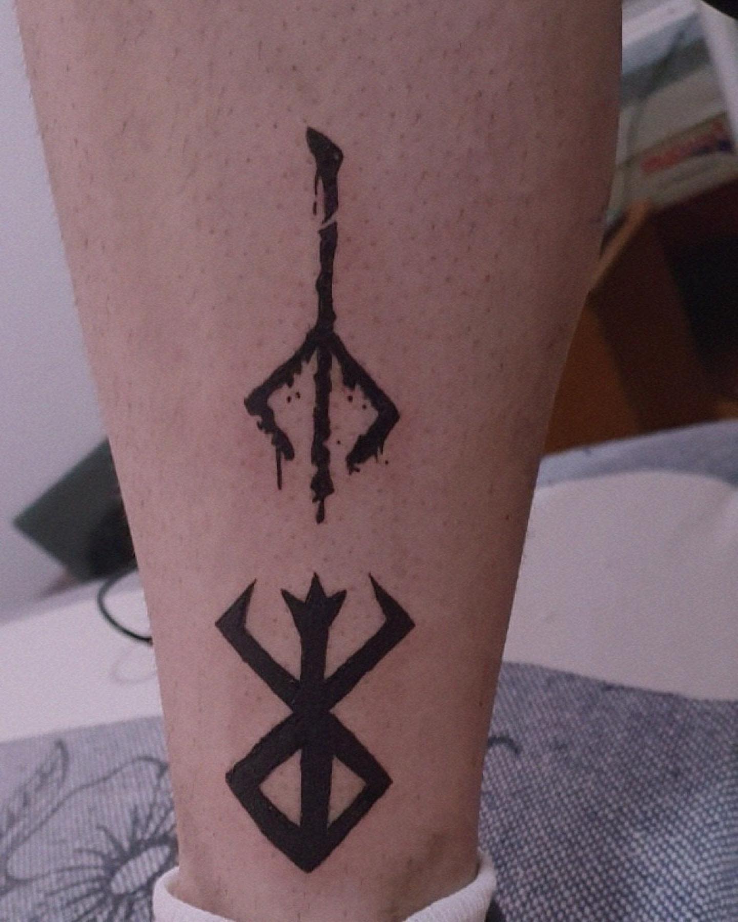Minimalist leg tattoo of the Bloodborne hunter's mark and a distinctive rune symbol in black ink